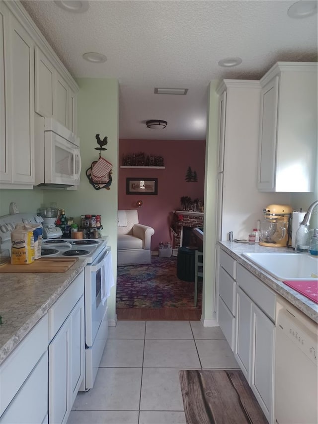 kitchen with white appliances, white cabinets, sink, light tile patterned floors, and a textured ceiling