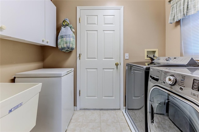 clothes washing area with washing machine and clothes dryer, light tile patterned flooring, and cabinets