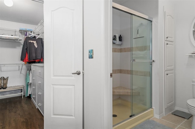 bathroom with wood-type flooring, toilet, and a shower with door