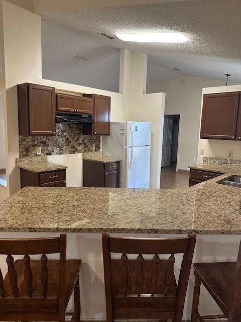 kitchen with white refrigerator, kitchen peninsula, a textured ceiling, and a breakfast bar area