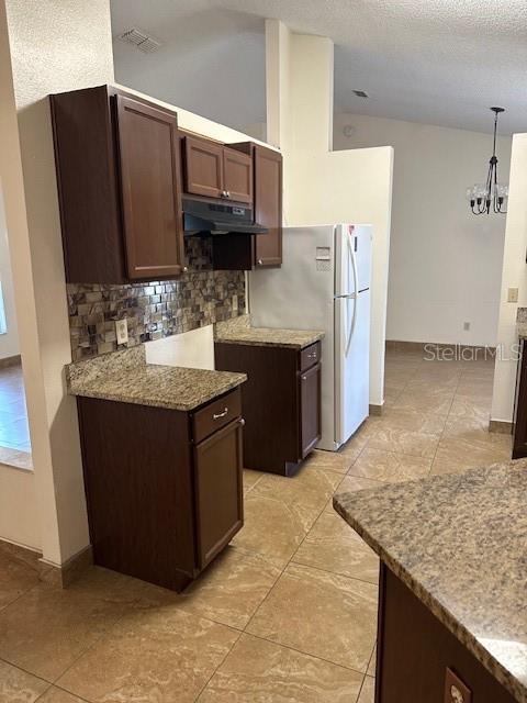 kitchen with dark brown cabinetry, stone counters, a notable chandelier, backsplash, and decorative light fixtures