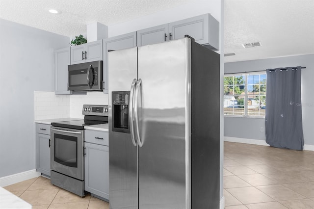 kitchen with appliances with stainless steel finishes, tasteful backsplash, light tile patterned floors, and gray cabinetry