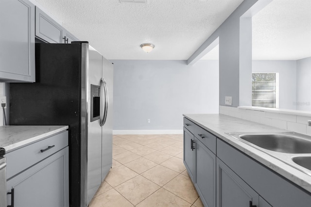 kitchen featuring stainless steel fridge, gray cabinetry, a textured ceiling, sink, and light tile patterned floors