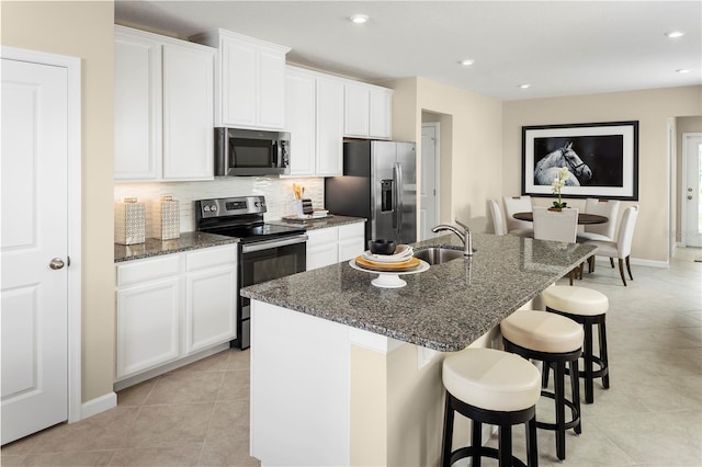 kitchen featuring white cabinetry, a kitchen island with sink, appliances with stainless steel finishes, and dark stone counters