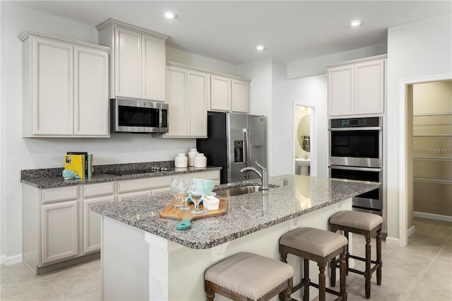 kitchen with sink, stainless steel appliances, a kitchen breakfast bar, dark stone counters, and a center island with sink