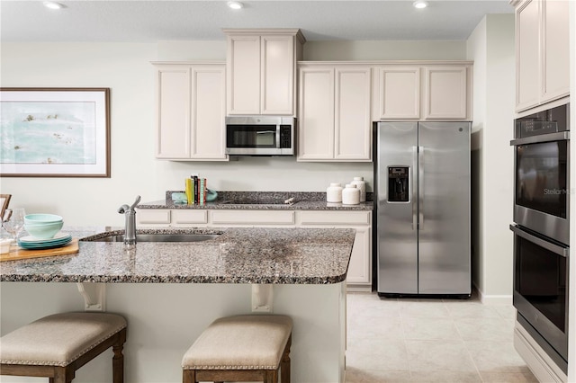 kitchen with white cabinets, a kitchen breakfast bar, sink, dark stone countertops, and stainless steel appliances