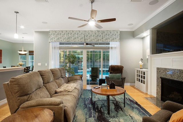 living room with french doors, ceiling fan, light wood-type flooring, ornamental molding, and a tiled fireplace