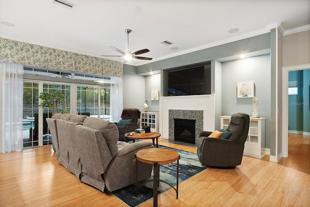 living room with ceiling fan, crown molding, light wood-type flooring, and a fireplace