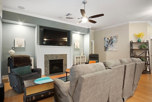 living room featuring crown molding, a fireplace, ceiling fan, and light hardwood / wood-style floors