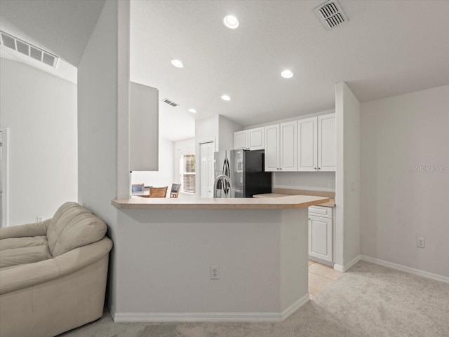 kitchen with stainless steel refrigerator, kitchen peninsula, and white cabinets