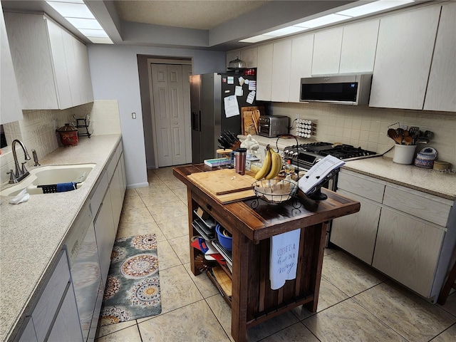 kitchen featuring backsplash, sink, light tile patterned floors, and stainless steel appliances