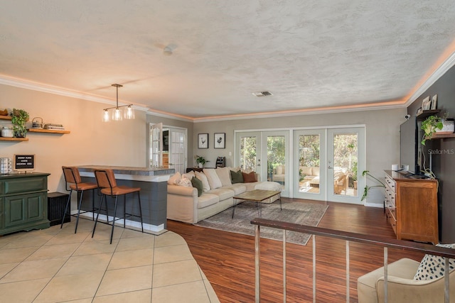 living room featuring french doors, light wood-type flooring, a textured ceiling, crown molding, and a chandelier