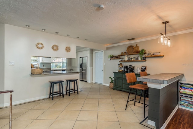 kitchen with a kitchen breakfast bar, stainless steel fridge, ornamental molding, light tile patterned flooring, and kitchen peninsula