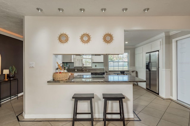 kitchen with dark stone counters, kitchen peninsula, stainless steel refrigerator with ice dispenser, light tile patterned floors, and white cabinetry