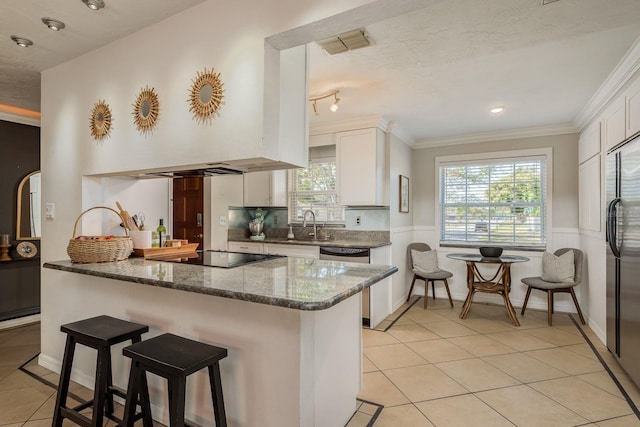 kitchen with kitchen peninsula, appliances with stainless steel finishes, light tile patterned floors, dark stone countertops, and white cabinetry