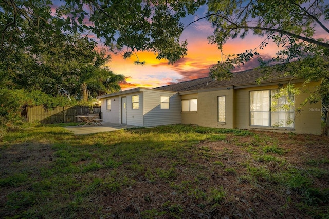 back house at dusk featuring a lawn and a patio