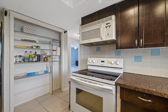 kitchen featuring tasteful backsplash, dark brown cabinets, white appliances, light tile patterned floors, and dark stone countertops