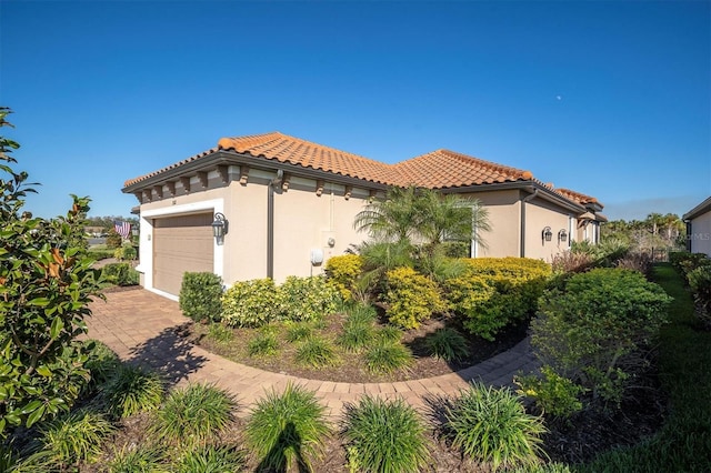 view of home's exterior featuring decorative driveway, a tiled roof, an attached garage, and stucco siding