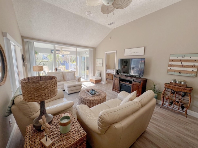 living room featuring a textured ceiling, light wood-type flooring, vaulted ceiling, and ceiling fan