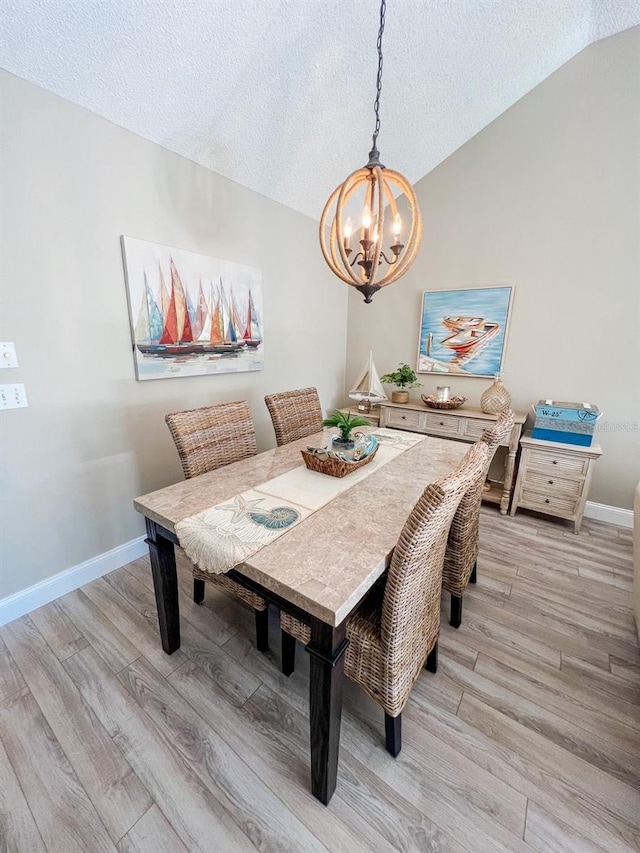 dining area featuring a chandelier, a textured ceiling, light hardwood / wood-style floors, and vaulted ceiling