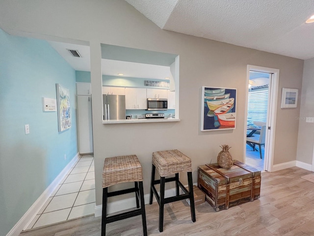 interior space with white cabinets, light hardwood / wood-style flooring, a textured ceiling, kitchen peninsula, and stainless steel appliances