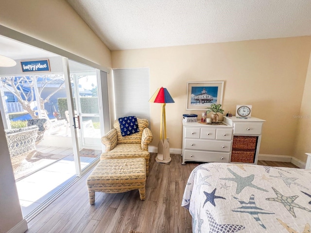 bedroom with access to exterior, wood-type flooring, a textured ceiling, and lofted ceiling