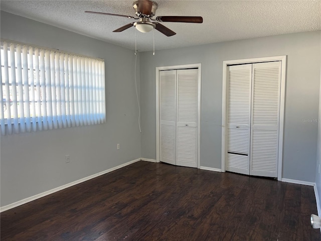 unfurnished bedroom featuring a textured ceiling, two closets, ceiling fan, and dark wood-type flooring