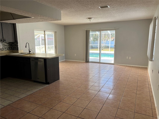 kitchen with sink, stainless steel dishwasher, kitchen peninsula, a textured ceiling, and light tile patterned floors