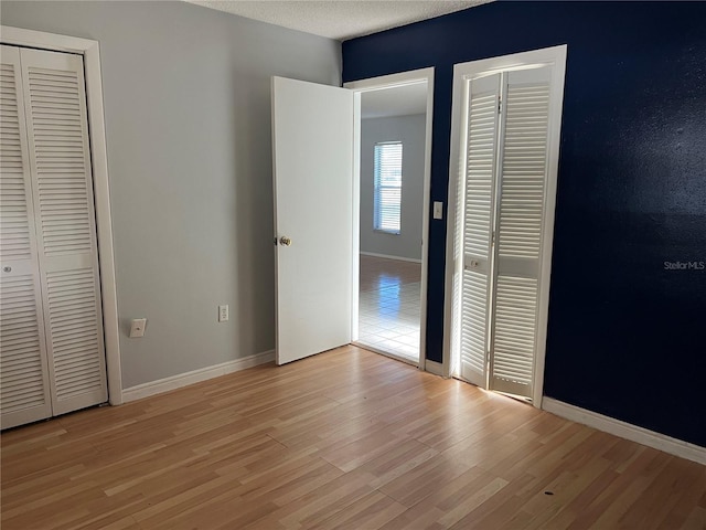 unfurnished bedroom featuring light hardwood / wood-style flooring, a textured ceiling, and multiple closets