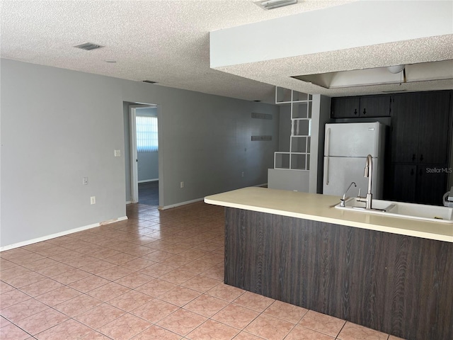 kitchen featuring a textured ceiling, white fridge, light tile patterned floors, and sink