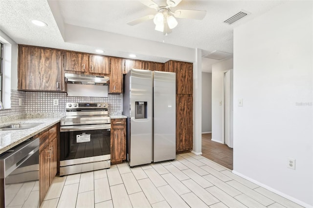 kitchen featuring decorative backsplash, appliances with stainless steel finishes, light stone counters, ceiling fan, and sink