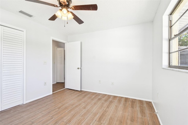 unfurnished bedroom featuring ceiling fan, light wood-type flooring, a textured ceiling, and a closet