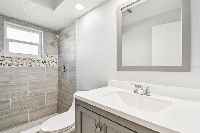 bathroom featuring tiled shower, vanity, and toilet