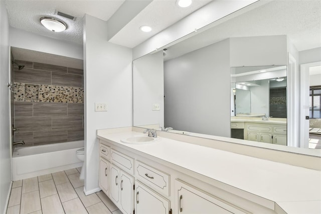 full bathroom with vanity, toilet, a textured ceiling, and tiled shower / bath combo