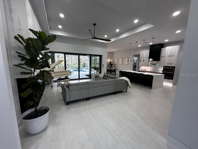 living room featuring a tray ceiling, ceiling fan, sink, and light hardwood / wood-style floors