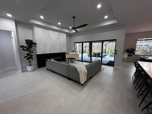 living room featuring a tray ceiling, a wealth of natural light, ceiling fan, and a fireplace