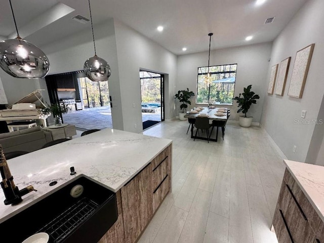 kitchen featuring light stone countertops, pendant lighting, and light hardwood / wood-style flooring