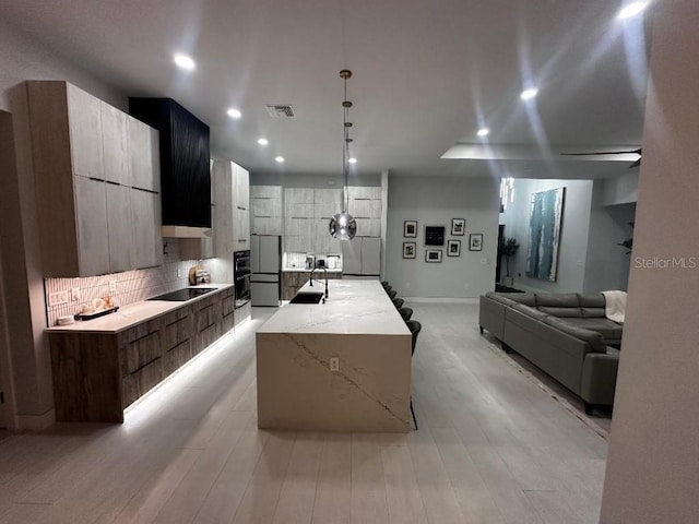 kitchen with light stone countertops, hanging light fixtures, tasteful backsplash, fridge, and a kitchen island with sink