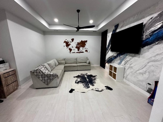 living room featuring light wood-type flooring, a tray ceiling, and ceiling fan