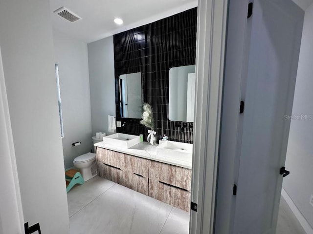 bathroom with tile patterned flooring, vanity, tasteful backsplash, and toilet