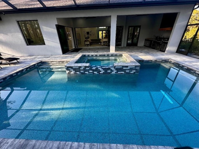 view of pool featuring an in ground hot tub, an outdoor kitchen, glass enclosure, and a patio area