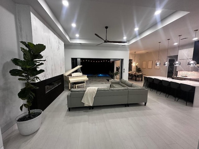 living room with ceiling fan with notable chandelier, light wood-type flooring, and a tray ceiling