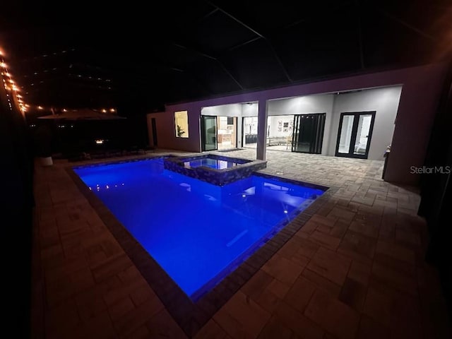 pool at night with a patio area, an in ground hot tub, and french doors