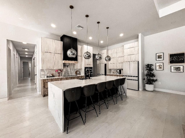 kitchen with light stone counters, a kitchen bar, an island with sink, and modern cabinets