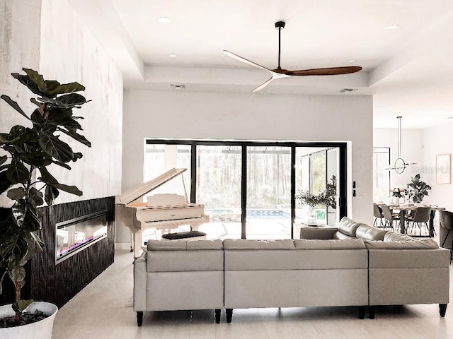 living room with ceiling fan, visible vents, a tray ceiling, and a glass covered fireplace