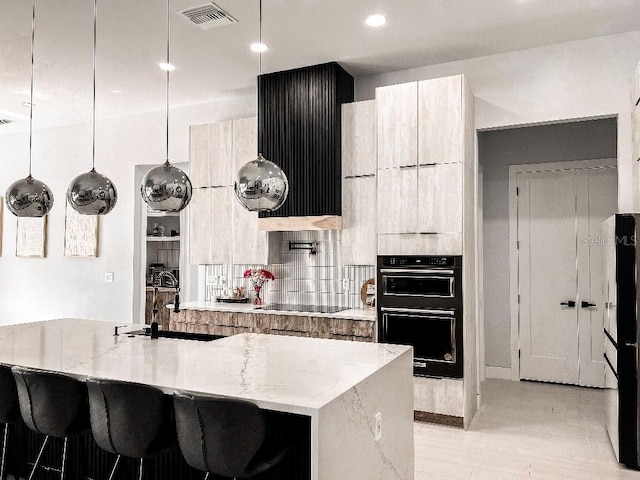 kitchen featuring modern cabinets, visible vents, hanging light fixtures, an island with sink, and light stone countertops