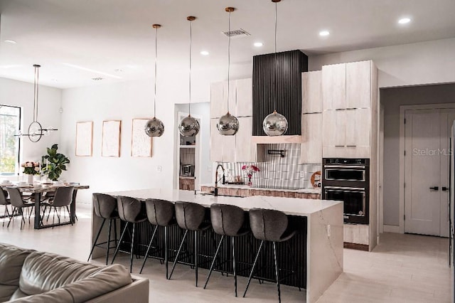 kitchen featuring a breakfast bar, an island with sink, modern cabinets, and dobule oven black