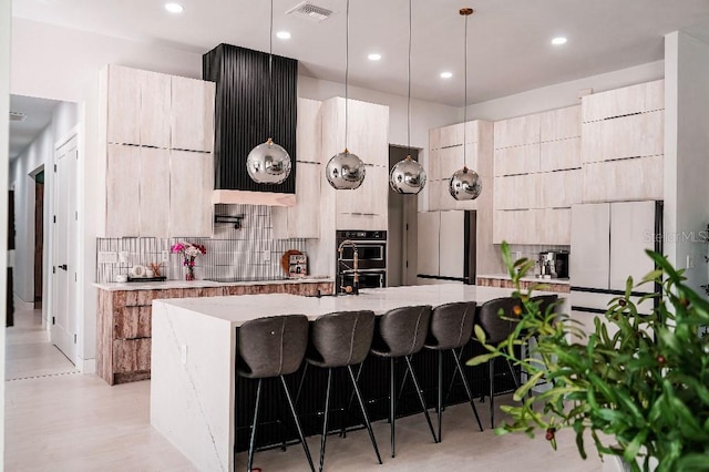 kitchen with visible vents, modern cabinets, light stone counters, a breakfast bar area, and a kitchen island with sink