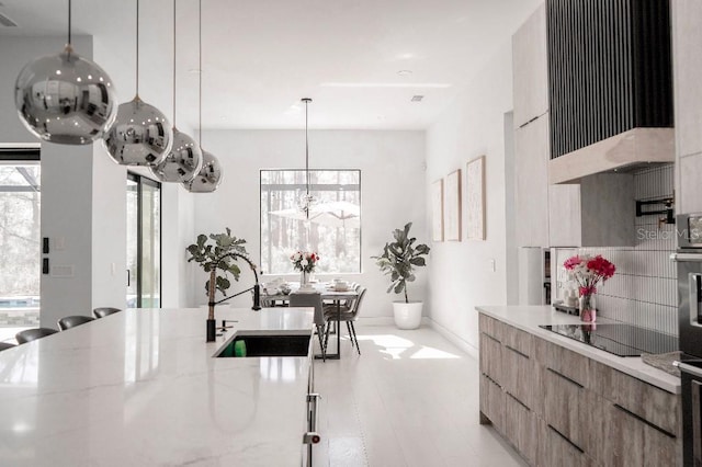 kitchen featuring modern cabinets, hanging light fixtures, light stone countertops, black appliances, and a sink