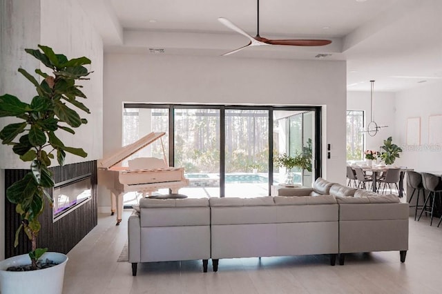 living area with a ceiling fan, a raised ceiling, and visible vents